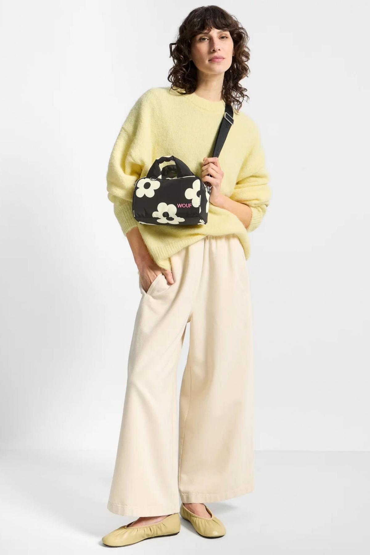 Bolso Wouf Night Daisy llevado cruzado, con estampado floral blanco sobre negro y formato bowling compacto