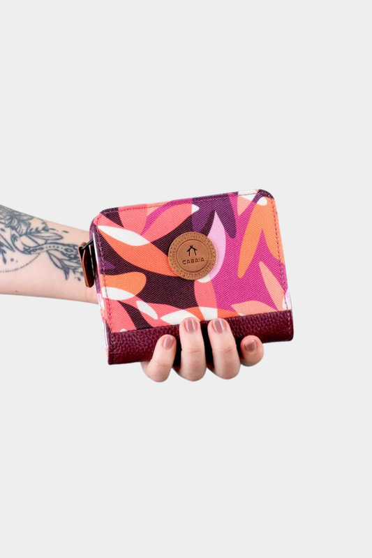 Cartera compacta Cabaia Small Montreuil mostrada en la mano con estampado burdeos y cierre completo de cremallera