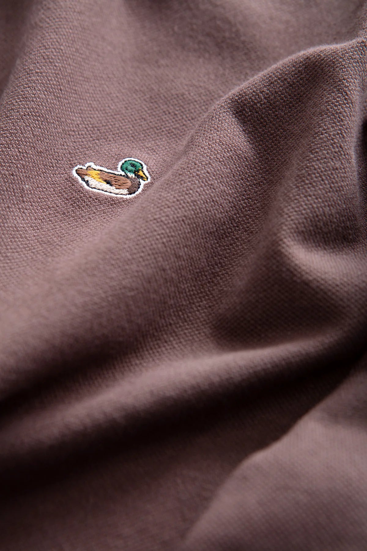 Detalle del polo marrón chocolate Edmmond Studios con cuello de botones y pequeño pato bordado en el pecho
